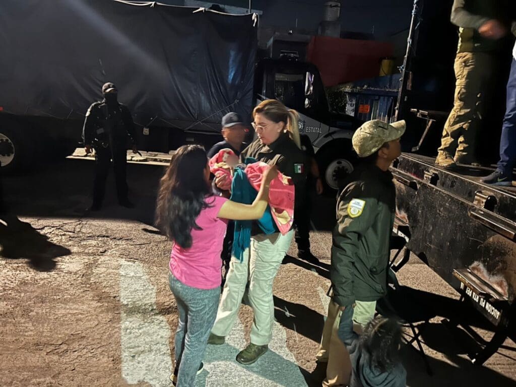 Imagen que muestra a una agente mexicana de migración sosteniendo a un bebé en medio de la interceptación de un tráiler con migrantes en el estado de Puebla.